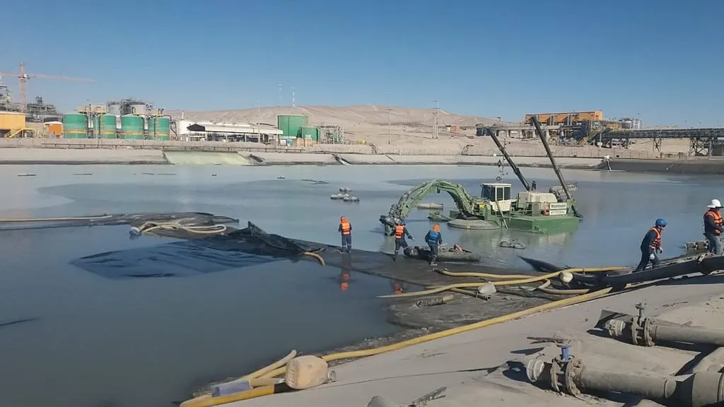 Equipo de dragado anfibio y personal especializado realizando trabajos de recuperación de sedimentos en un tranque minero industrial.