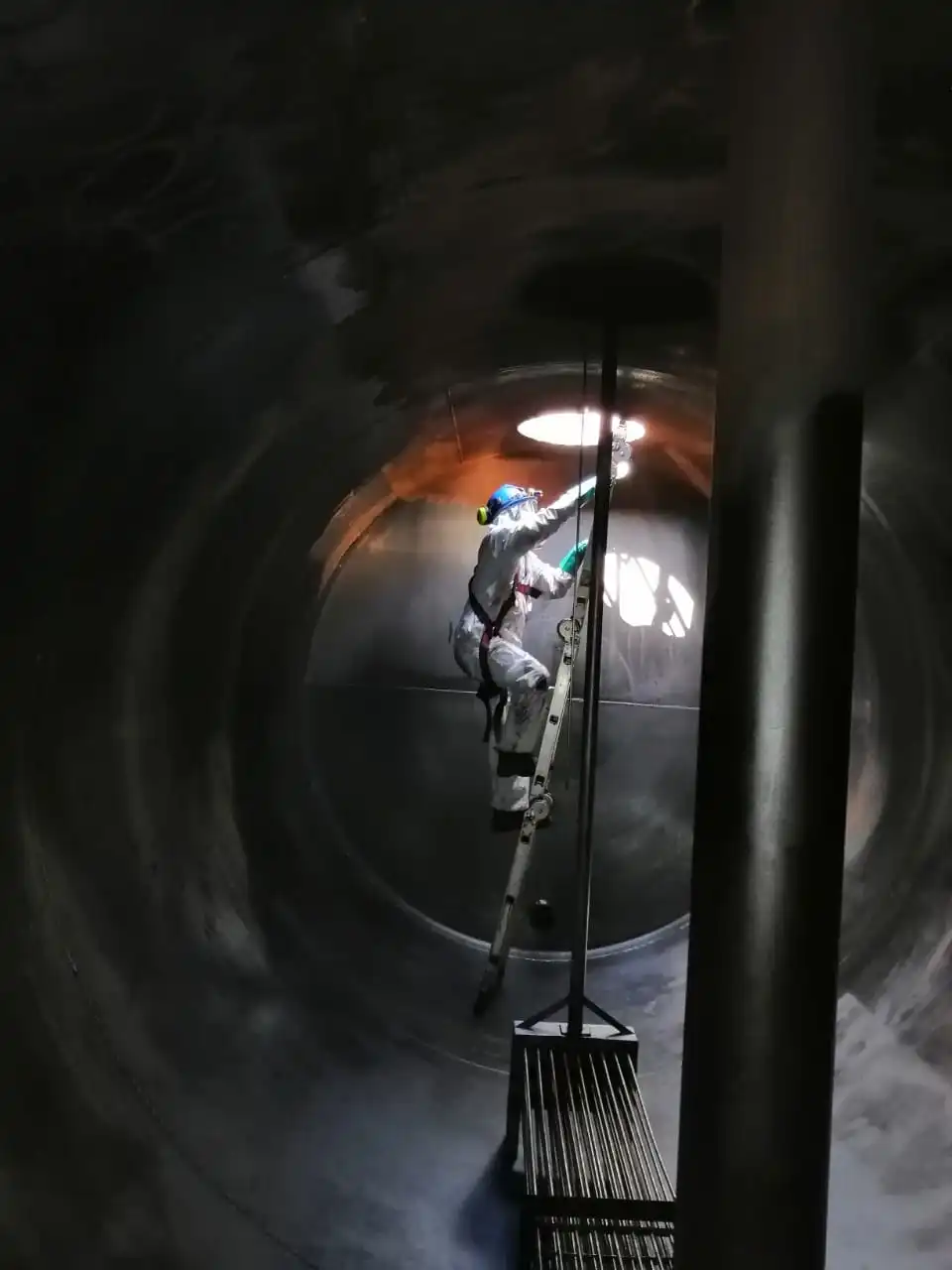 Trabajador equipado con elementos de protección realizando mantenimiento y limpieza al interior de una piscina PLS utilizada en procesos de extracción de cobre.