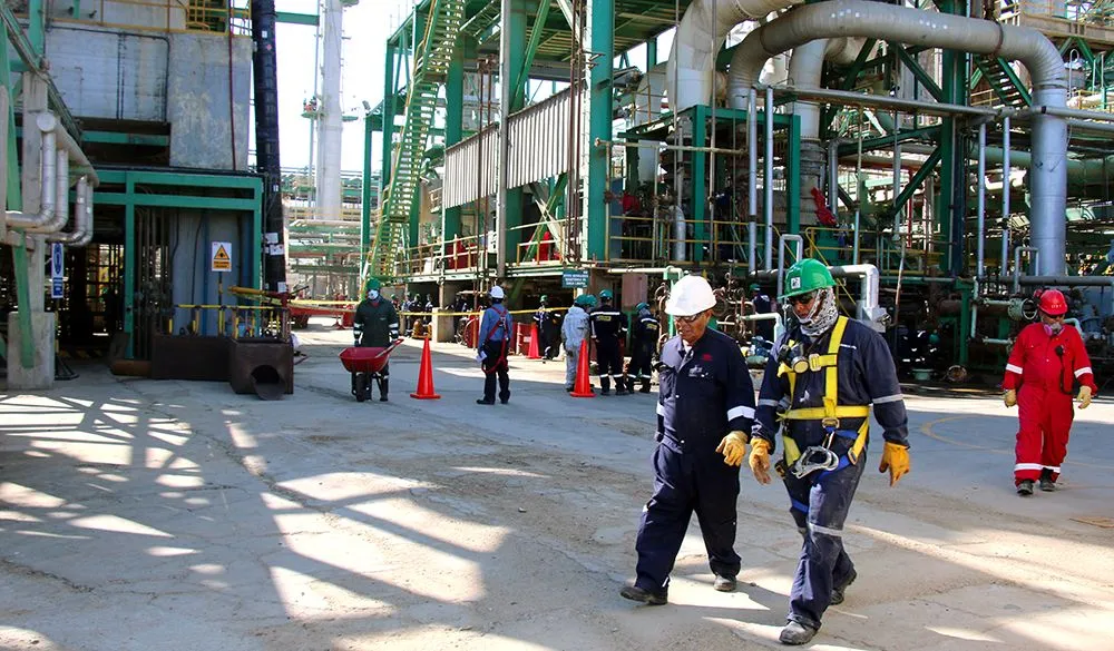 Trabajadores equipados con elementos de protección personal recorriendo una planta industrial durante labores de mantenimiento y supervisión.